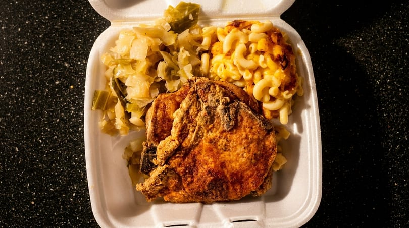 Fried pork chop, macaroni and cheese, and cabbage in a white takeout container.
