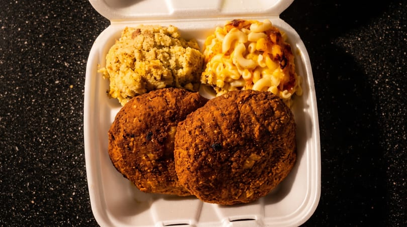 Takeout container with two fried patties, macaroni and cheese, and cornbread dressing.