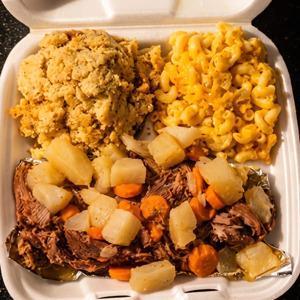 A takeout container with pot roast, potatoes, carrots, cornbread dressing, and macaroni and cheese.