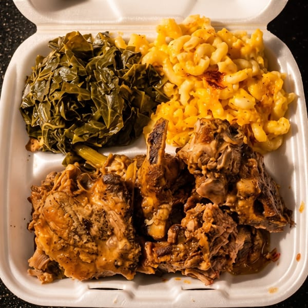 A takeout container filled with collard greens, macaroni and cheese, and smothered turkey wings.