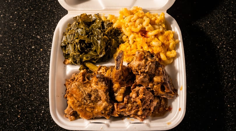 A takeout container filled with collard greens, macaroni and cheese, and smothered turkey wings.
