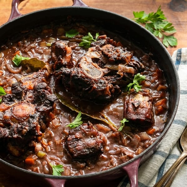 Oxtail stew with vegetables and herbs in a cast iron pot on a wooden table.